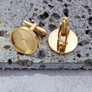 Può includere: Un paio di gemelli dorati con una superficie rotonda e liscia. I gemelli hanno un design semplice e classico.