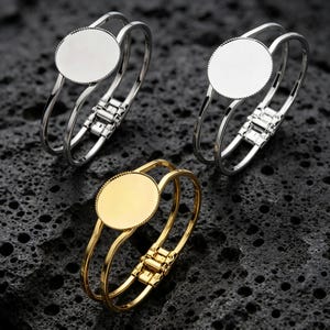 May include: Three hinged cuff bracelets, two in silver-tone and one in gold-tone metal. Each bracelet features a double-band design and a central circular blank bezel setting with a textured, beaded edge, designed for customisation or jewellery making.