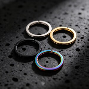 May include: Four circular metal rings arranged in a cluster. The set includes one silver-toned ring, one gold-toned ring, one matte black ring, and one iridescent rainbow-colored ring. Each ring features a small split opening along the band.