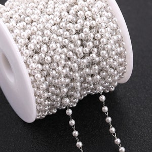 May include: A spool of white pearl chain, a type of jewellery making supply. The chain is made of small white beads strung on a silver chain.