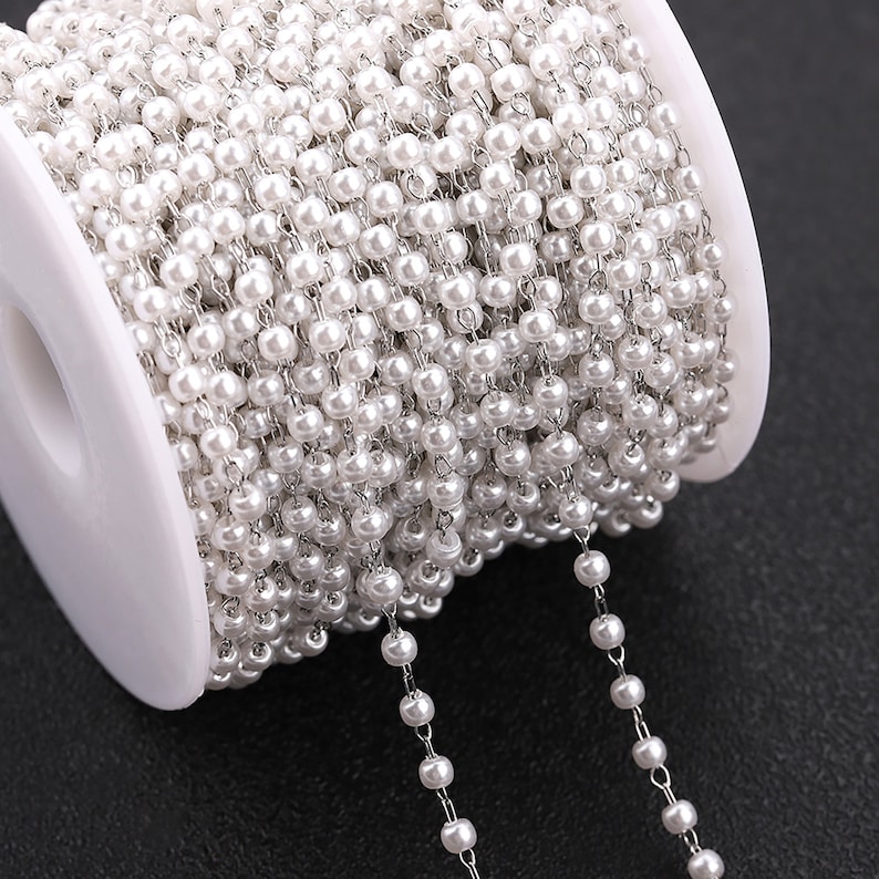 May include: A spool of white pearl chain, a type of jewellery making supply. The chain is made of small white beads strung on a silver chain.