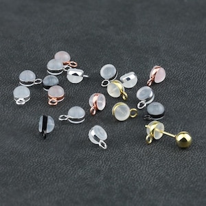 Könnte beinhalten: Sortiment aus kleinen, runden, klaren Glasperlen mit silbernen, goldenen und roségoldenen Metallschleifen. Die Perlen sind auf einer dunkelgrauen Oberfläche verstreut.