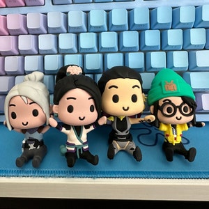 Könnte beinhalten: Vier kleine, farbenfrohe Figuren mit Comic-artigen Merkmalen. Die Figuren sind aus Kunststoff und haben einen Chibi-Stil. Die Figuren sitzen auf einer blauen Oberfläche.