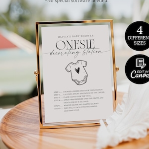 Könnte beinhalten: Ein goldgerahmtes Schild für eine Babyparty mit dem Text "Olivia's Baby Shower Onesie Decorating Station". Das Schild enthält eine Zeichnung eines Stramplers mit einem Herz und Anweisungen. Zusätzlicher Text lautet "4 Verschiedene Größen" und "Edit in Canva".