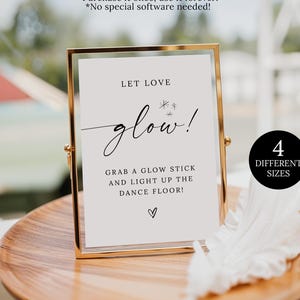 May include: A gold-framed sign with the words "LET LOVE glow!" in elegant script. The sign also includes the text "GRAB A GLOW STICK AND LIGHT UP THE DANCE FLOOR!" and a heart symbol. A black circle indicates "4 DIFFERENT SIZES".