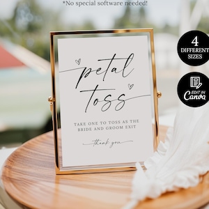 Op de afbeelding: Een verticaal rechthoekig bord in een goudkleurig metalen frame met de zwarte tekst petal toss, take one to toss as the bride and groom exit en thank you. Het bord bevat twee kleine hartjes en staat op een rond houten bord.