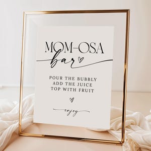 May include: A printable sign in a gold frame with the text "MOM-OSA bar" and instructions for making a mimosa: "POUR THE BUBBLY ADD THE JUICE TOP WITH FRUIT enjoy".