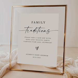 May include: A white sign with a gold frame, with the text "FAMILY Traditions" in black script. The sign instructs guests to write down their favorite family tradition from their childhood. The sign also includes the text "AUDREY'S BABY SHOWER 09.24.20XX".