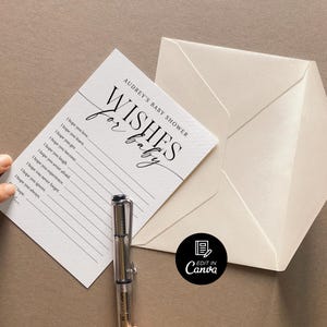以下が含まれることがあります： 白いカードに黒い文字で「Audrey's Baby Shower Wishes for Baby」と書かれています。カードには、赤ちゃんへの願い事を書くための線が引かれています。カードの上にペンが置かれています。カードは白い封筒の上に置かれています。