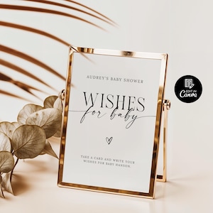 以下が含まれることがあります： 金色の額縁に「Audrey's Baby Shower Wishes for Baby」という黒い筆記体で書かれた文字が入った看板。看板には「Take a card and write your wishes for Baby Hanson.」という文字も書かれている。