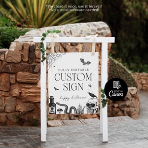 May include: A white wooden sign with a Halloween theme. The sign reads "CUSTOM SIGN" with decorative illustrations of a bat, spider, skull, and snake. The sign is decorated with greenery and is set outdoors.