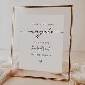 Puede incluir: Un cartel blanco en un marco dorado con el texto "Here's to our angels. They have the best seat in the house." con un pequeño símbolo de corazón en la parte inferior.
