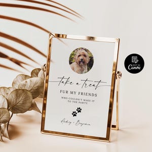 May include: A white sign with black text that reads "take a treat FUR MY FRIENDS WHO COULDN'T MAKE IT TO THE PAWTY" with a paw print graphic and the names "Audrey & Benjamin". A photo of a dog is in the top left corner of the sign. The sign is in a gold frame.