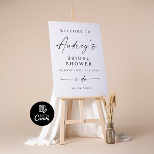 Puede incluir: Un letrero blanco sobre un caballete de madera con el texto "Welcome to Audrey's Bridal Shower" en elegante escritura negra. El letrero tambi&eacute;n incluye la fecha "09.24.20XX" y la frase "24 d&iacute;as hasta que diga que s&iacute;."