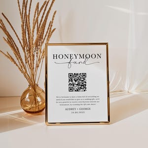 Puede incluir: Un cartel con marco dorado con el texto "Honeymoon Fund" en letra cursiva negra. Debajo del texto se muestra un c&oacute;digo QR en blanco y negro. El cartel tambi&eacute;n incluye el texto "We're fortunate to have a home full of everything we need. If you would like to give us a wedding gift, we'd be very grateful to receive contributions towards our honeymoon, by scanning the QR code above! Audrey + George 24.08.20XX"