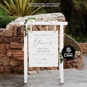 Puede incluir: Un letrero blanco con el texto "WELCOME TO Olivia's BRIDAL SHOWER 24 DAYS UNTIL SHE SAYS I do 09.24.20XX". El letrero est&aacute; sostenido por un marco de madera blanco y decorado con vegetaci&oacute;n, sobre un muro de piedra.
