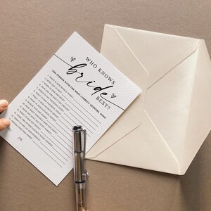 May include: A white card with black text that says "Who Knows the Bride Best?" with a list of questions about the bride. The card is on a beige surface with a white envelope.