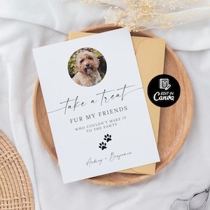 May include: White card with black text that reads "Take a treat fur my friends who couldn't make it to the pawty."  The card has a paw print graphic and a photo of a golden dog in a circle. The text "Anticy + Benjamin" is at the bottom of the card.  The card is on a brown wooden surface.