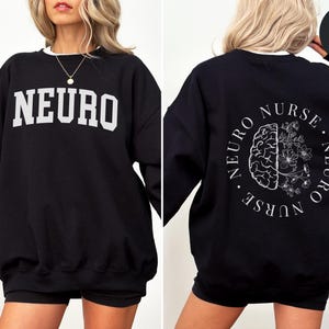 K&ouml;nnte beinhalten: Schwarzes Sweatshirt mit wei&szlig;em Besatz. Auf der Vorderseite steht das Wort "NEURO" in wei&szlig;en Buchstaben. Auf der R&uuml;ckseite befindet sich ein kreisf&ouml;rmiges Design mit "NEURO NURSE" und einer Gehirngrafik mit floralen Elementen.