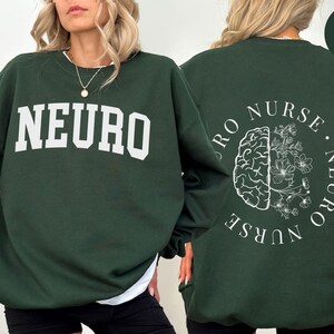 K&ouml;nnte beinhalten: Forstgr&uuml;nes Sweatshirt mit dem Wort "NEURO" in Wei&szlig; auf der Vorderseite. Auf der R&uuml;ckseite befindet sich eine Gehirngrafik mit Blumen und den Worten "NEURO NURSE" in einem Kreis. Ein l&auml;ssiges, bequemes Kleidungsst&uuml;ck.