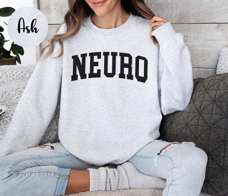K&ouml;nnte beinhalten: Hellgraues Sweatshirt mit dem Wort "NEURO" in fetten, schwarzen Buchstaben auf der Brust. Das Sweatshirt hat einen Rundhalsausschnitt und lange &Auml;rmel. Das Model tr&auml;gt eine hellblaue Jeans.