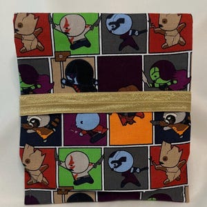 May include: A fabric item featuring a repeating pattern of cartoon characters in a grid. The characters are in various colors, including red, green, and blue. A gold elastic band wraps around the item.