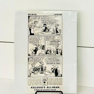 May include: A framed black and white comic strip titled "Mutt and Jeff" by Bud Fisher. The comic strip promotes Kellogg's All-Bran cereal. The image is displayed on a black metal stand against a white background.