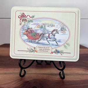 May include: A rectangular, off-white metal tray with a Christmas scene featuring a horse-drawn sleigh. The tray has a decorative border and the text "Celebrate the special magic of Christmas in the Heartland."