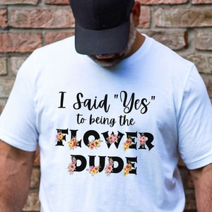 May include: White t-shirt with the text "I said "Yes" to being the FLOWER DUDE" in black with floral accents.