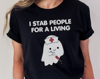 May include: Black t-shirt with the text "I STAB PEOPLE FOR A LIVING". The shirt features a cartoon ghost wearing a nurse's hat and holding a syringe. The ghost has a smiling face and the syringe contains red liquid.