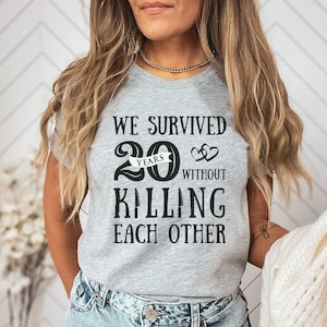 K&ouml;nnte beinhalten: Graues T-Shirt mit dem Text "We survived 20 years without killing each other" und zwei ineinander verschlungenen Herzen.
