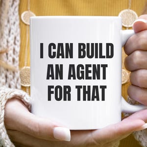 May include: A white ceramic mug featuring the black text I CAN BUILD AN AGENT FOR THAT printed in a bold, sans-serif font on the front. The mug has a standard cylindrical shape with a curved handle on the right side for holding.