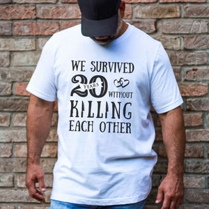 K&ouml;nnte beinhalten: Wei&szlig;es T-Shirt mit schwarzem Text, der "We survived 20 years without killing each other" lautet. Die Zahl 20 ist in einer gro&szlig;en, fetten Schriftart mit dem Wort "years" in einer kleineren Schriftart dar&uuml;ber. Zwei kleine Herzen befinden sich rechts neben der Zahl 20.