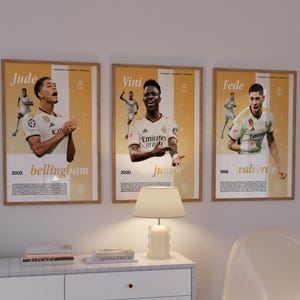 May include: Three framed posters of Real Madrid soccer players. Each poster features a player's name, year of birth, and a photo of the player in their team uniform. The posters are in a light wood frame with a white background and gold accents.