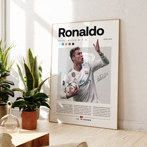 May include: A white and gray poster with a photo of Cristiano Ronaldo playing soccer for Real Madrid. The poster has the text "Ronaldo", "Real Madrid F.C.", "2009-2018", "Fly Emirates", and "Rate 91*****".