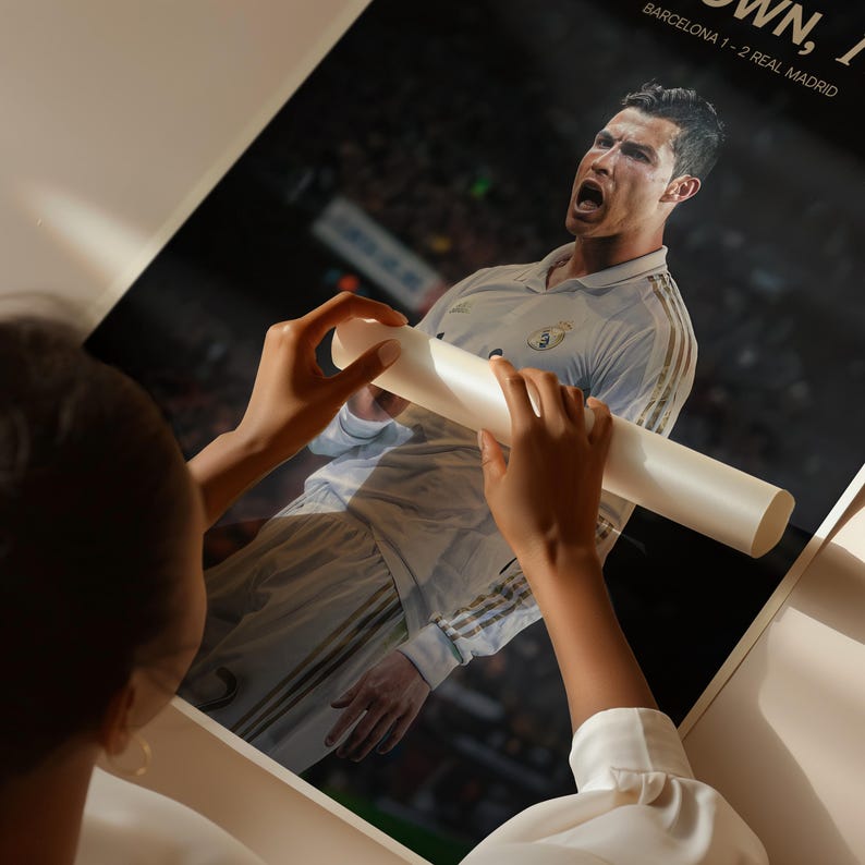 May include: A poster featuring a soccer player in a white jersey, with the text "BARCELONA 1-2 REAL MADRID" visible. The poster is being held by a person.