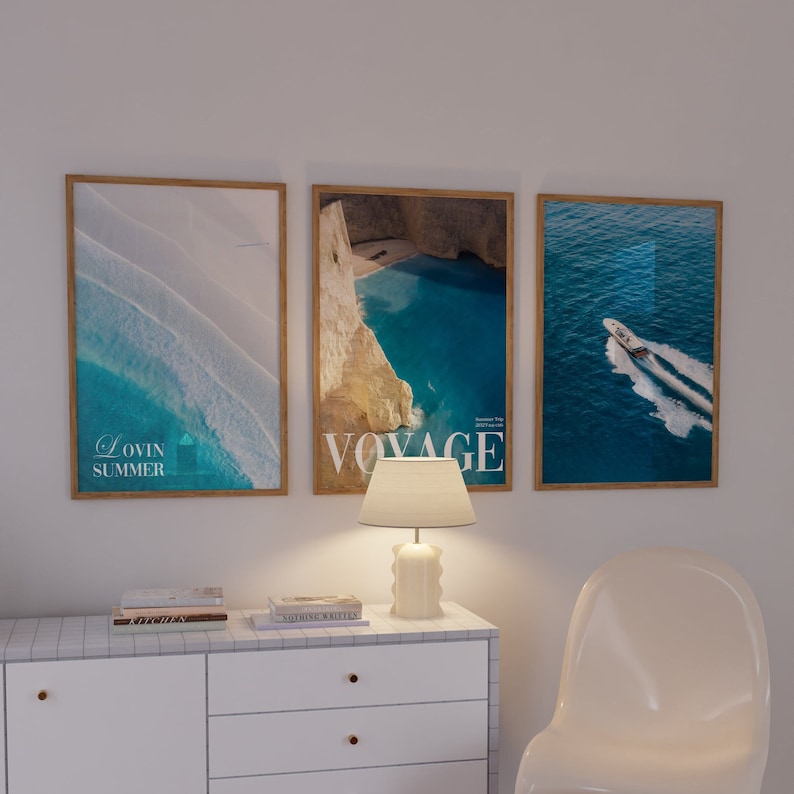 K&ouml;nnte beinhalten: Drei gerahmte Drucke mit Strandthema. Der linke Druck hat ein blaues und wei&szlig;es abstraktes Design mit dem Text "Lovin Summer". Der mittlere Druck zeigt eine Bucht mit t&uuml;rkisfarbenem Wasser und dem Text "Voyage". Der rechte Druck zeigt ein Boot auf dem Meer mit blauem Wasser.