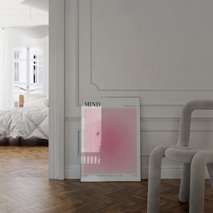 May include: A framed poster with the word "MIND" at the top, featuring a gradient of pink hues. The poster includes the text "Apollo Studio" and a quote at the bottom. A modern, light gray chair is to the right.