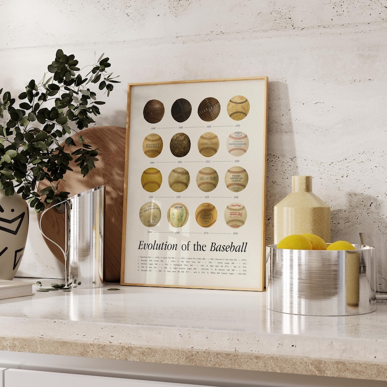May include: A framed print titled "Evolution of the Baseball" displays a series of baseballs from different eras. The baseballs are arranged in rows, illustrating their development over time. The print has a beige background and a wooden frame.