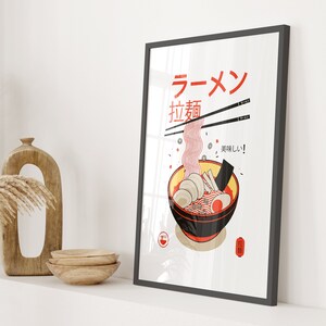 Puede incluir: Un p&oacute;ster enmarcado con una ilustraci&oacute;n roja y blanca de un taz&oacute;n de fideos ramen. El p&oacute;ster tiene las palabras japonesas "Ramen" y "拉麺" (Ramen) en rojo y negro. El texto "美味しい!" (&iexcl;Delicioso!) est&aacute; en negro. El p&oacute;ster tiene un sello rojo y blanco con la palabra japonesa "拉麺" (Ramen) en negro.