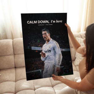 May include: A black poster featuring a soccer player in a white jersey. The poster has the text "CALM DOWN, I'm here" and "BARCELONA 1 - 2 REAL MADRID" in white. The player is wearing a jersey with the word "win".