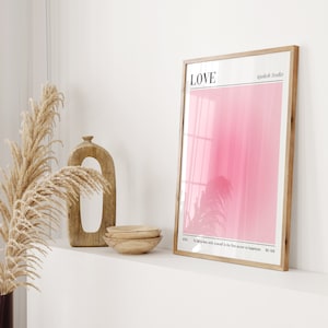 May include: A framed art print with a pink gradient background and the word "LOVE" at the top. The print also includes the text "To fall in love with yourself is the first secret to happiness." Decorative wooden bowls and a wooden sculpture are also visible.