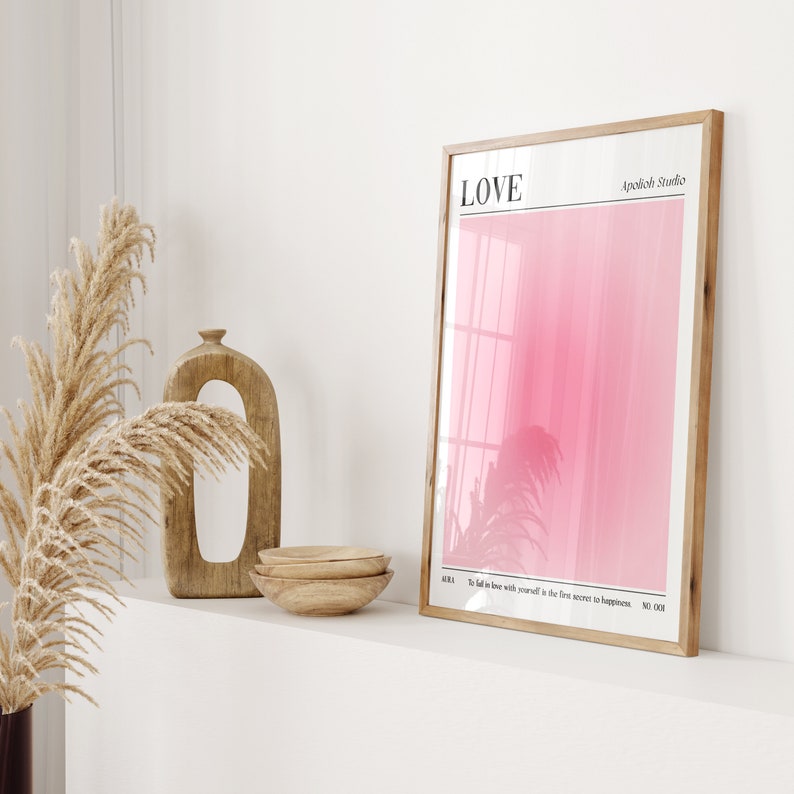 May include: A framed art print with a pink gradient background and the word "LOVE" at the top. The print also includes the text "To fall in love with yourself is the first secret to happiness." Decorative wooden bowls and a wooden sculpture are also visible.