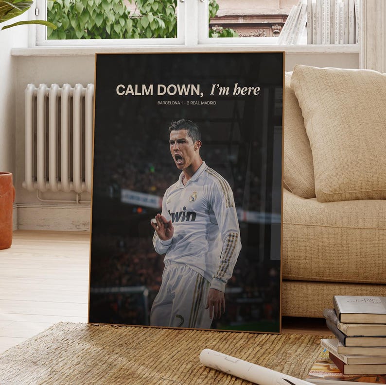 May include: A framed poster with a football player in a white jersey. The poster has the text "CALM DOWN, I'm here" and "BARCELONA 1-2 REAL MADRID" in white font against a black background. The player is gesturing with his hand.