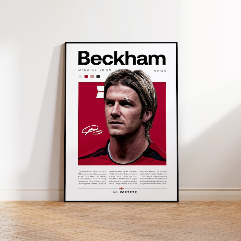 May include: A red and white poster with a black border featuring a photo of David Beckham, a former professional footballer. The poster has the text "Beckham" in large black letters at the top and "Manchester United 1991-2003" in smaller black letters below. The poster also includes a small signature in red ink.