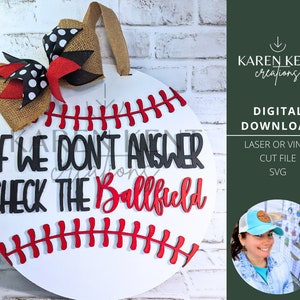 May include: White round wooden door hanger with a red and black bow, red stitching, and the text "IF WE DON'T ANSWER CHECK THE BALLFIELD".