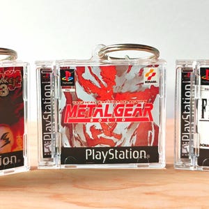Puede incluir: Tres llaveros de carcasas de juegos de PlayStation. Los llaveros presentan los títulos de los juegos Tekken 3, Metal Gear Solid y Final Fantasy VII. Cada estuche tiene un llavero plateado.
