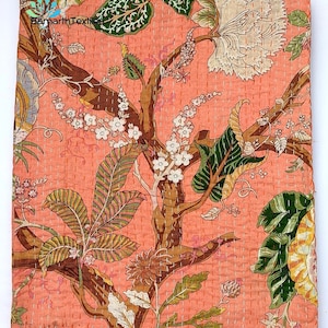 May include: A peach-coloured kantha quilt with a floral pattern. The quilt features a large tree with brown branches and green leaves, as well as white flowers. The quilt is hand-stitched and has a delicate, intricate design.