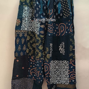 May include: Blue patchwork pants with a variety of floral and geometric patterns. The pants have an elastic waistband and a drawstring. The pants are made of cotton and are comfortable to wear. "Samarth Textiles" is printed on the pants.