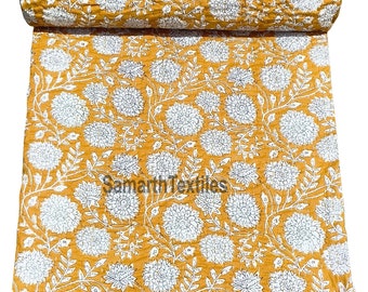 May include: A yellow kantha quilt with a white floral pattern. The quilt is folded and rolled up, showing the intricate stitching and design.